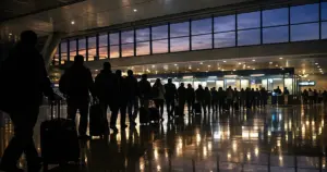 Long queue of silhouetted travelers in airport arrivals hall with immigration booths in distance