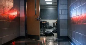 University classroom door ajar with scattered belongings and overturned furniture visible inside under emergency lighting