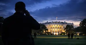 Secret Service agent silhouette monitoring White House South Lawn at dusk with illuminated mansion in background