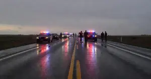 Emergency vehicles with flashing lights on a wet rural highway at dusk with first responders in silhouette