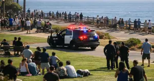Police vehicle with emergency lights active in crowded seaside park with ocean in background