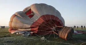 Hot air balloon deflating and collapsing on the ground at dawn with basket tipped over