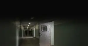 Heavy steel prison cell door in dimly lit institutional corridor with reinforced window