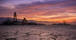 Black Rock Desert playa at dusk with distant festival structures silhouetted against purple sky