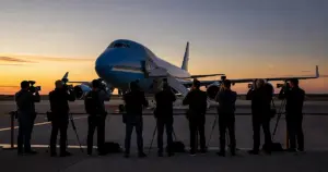 Press photographers silhouetted at barrier facing Air Force One on tarmac at dusk