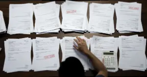 Medical billing documents and collection notices scattered on office desk with silhouetted hand reviewing papers