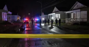 Police tape and emergency vehicle lights illuminate a residential street at night with silhouetted officers