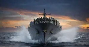 Navy warship deck cutting through ocean water at dusk with silhouetted sailors at stations